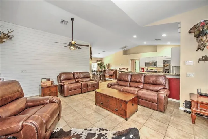 Tiled living room with ceiling fan and vaulted ceiling with planters shelves.
