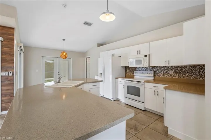 Kitchen with white cabinets, white appliances, hanging light fixtures, an island with sink, and vaulted ceiling