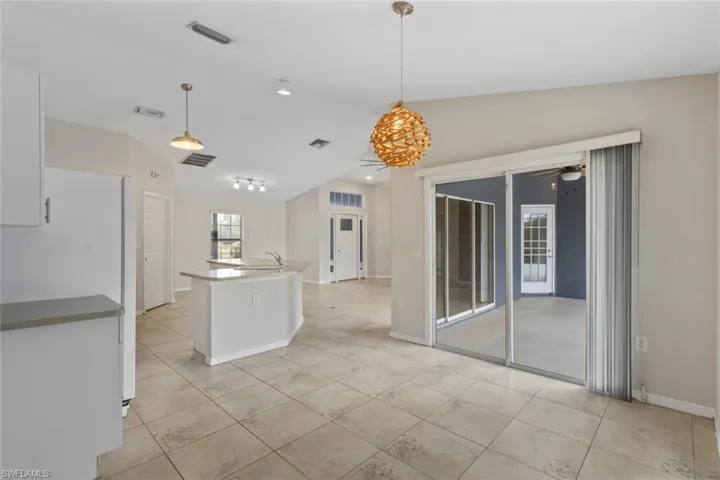 Kitchen with hanging light fixtures, white cabinets, ceiling fan, freestanding refrigerator, and a kitchen island with sink