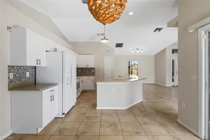 Kitchen with tasteful backsplash, white cabinets, pendant lighting, white appliances, and lofted ceiling