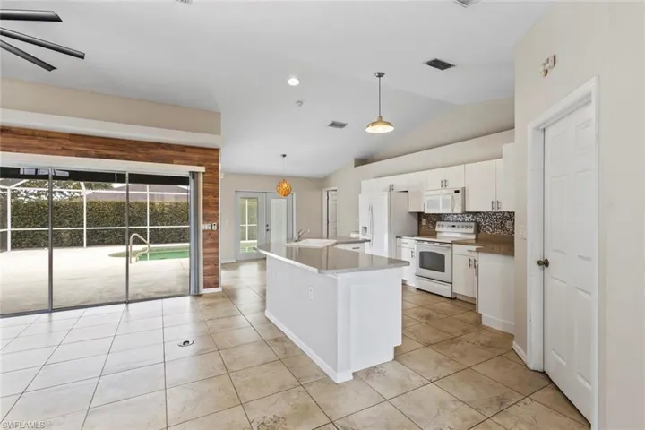 Kitchen featuring white cabinets, white appliances, a kitchen island with sink, vaulted ceiling, and pendant lighting