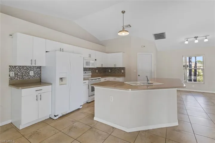 Kitchen featuring backsplash, white appliances, white cabinetry, an island with sink, and light tile patterned floors