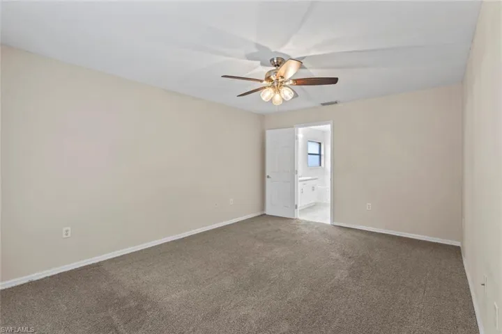 Carpeted Primary bedroom with baseboards and ceiling fan facing primary bath