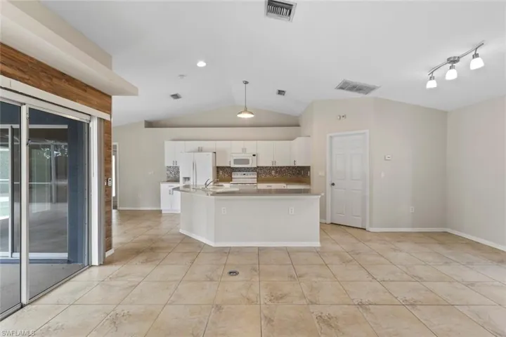 Kitchen with white appliances, white cabinets, backsplash, pendant lighting, and an island with sink