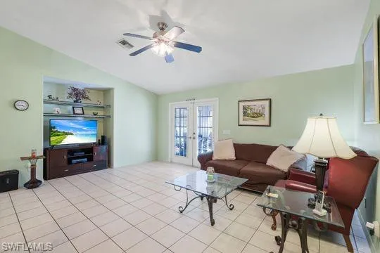 Living area featuring built in shelves, french doors, lofted ceiling, visible vents, and ceiling fan