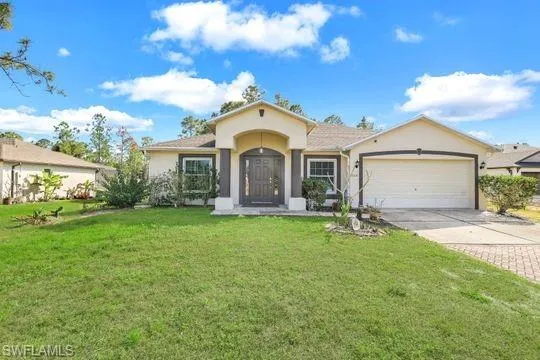 View of front of house featuring a garage, driveway, a front lawn, and stucco siding
