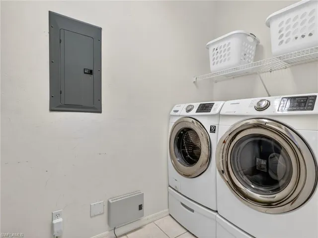 Laundry room with electric panel, washing machine and dryer, and light tile patterned floors