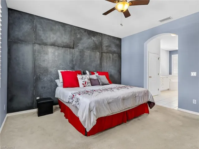 Bedroom featuring light colored carpet, arched walkways, a ceiling fan, ensuite bath, and an accent wall