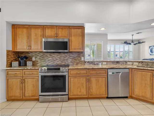 Kitchen featuring stainless steel appliances, light granite counters, wood finish cabinets, light tile patterned flooring, and recessed lighting