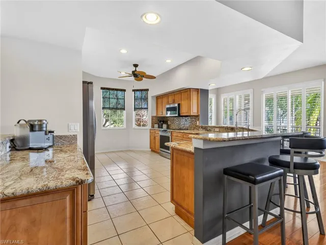 Kitchen with wood finish cabinetry, light granite counters, stainless steel appliances, ceiling fan, and light tile patterned floors