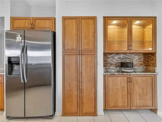 Kitchen with stainless steel fridge, tasteful backsplash, light granite countertops, and wood finish cabinetry