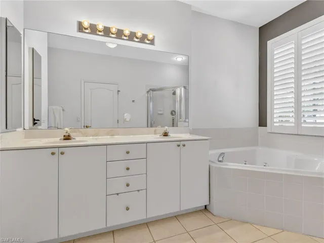 Bathroom featuring double vanity, a shower stall, light tile patterned floors, and a bath