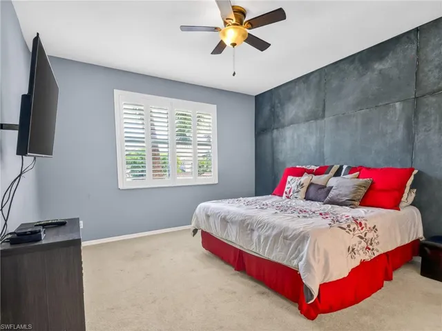 Bedroom with light colored carpet, an accent wall, and ceiling fan