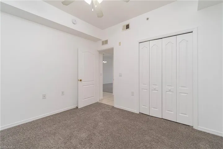 Unfurnished bedroom with ceiling fan, carpet flooring, visible vents, and a closet