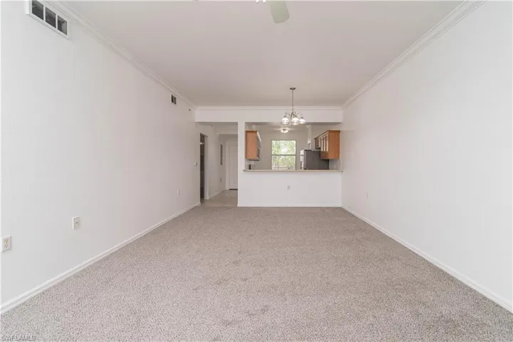 Unfurnished living room featuring visible vents, crown molding, baseboards, light colored carpet, and ceiling fan with notable chandelier