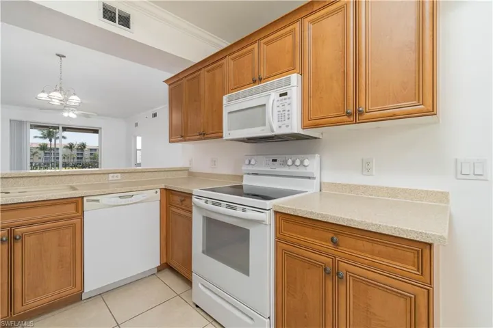 Kitchen featuring brown cabinets, white appliances, a chandelier, and ornamental molding