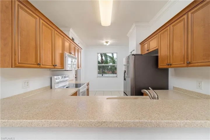 Kitchen featuring crown molding, a sink, brown cabinets, white appliances, and light countertops