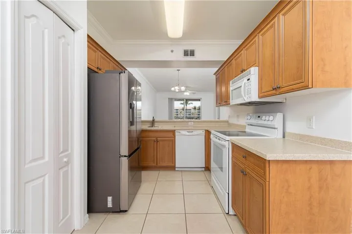 Kitchen with visible vents, an inviting chandelier, white appliances, brown cabinetry, and ornamental molding