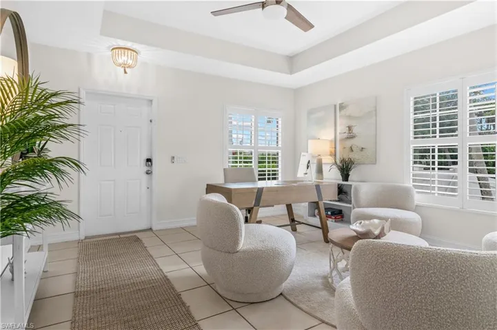 Entryway and office area in living room featuring a white four-panel door, tray ceiling, and neutral tile flooring