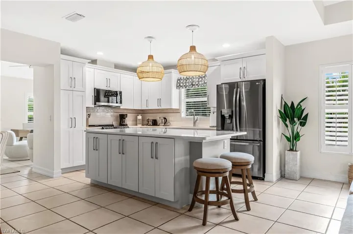 Contemporary kitchen featuring a center island with pendant lighting, white shaker-style cabinetry, stainless steel appliances, and tile flooring