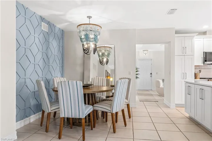 Dining area featuring a geometric accent wall, two decorative chandeliers, and tile flooring