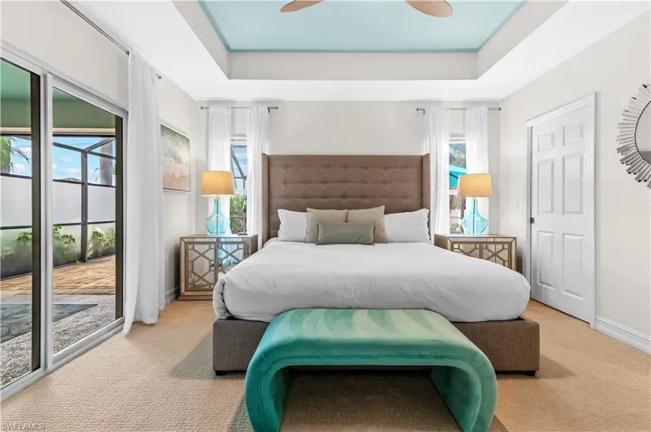 Carpeted room featuring a light blue tray ceiling with a ceiling fan, a paneled door, and sliding glass doors opening to an outdoor area