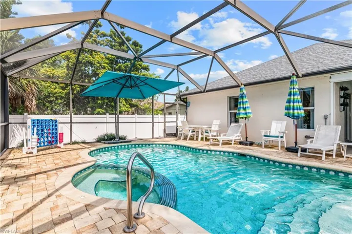 Screened pool enclosure featuring an integrated spa with a curved entry, surrounded by paver decking and a white perimeter fence