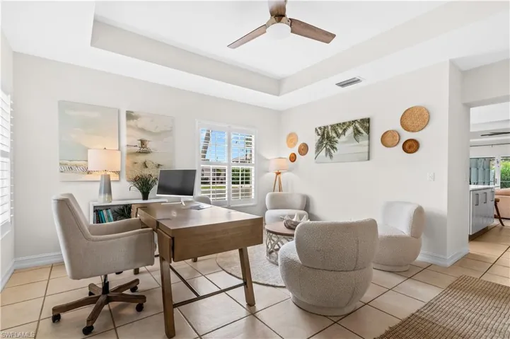 Bright interior space featuring a tray ceiling with a ceiling fan, tile flooring, and plantation shutters