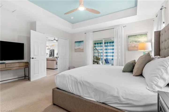 Carpeted bedroom featuring a tray ceiling with a ceiling fan, direct patio access via sliding glass doors, white paneled double doors, and a built-in entertainment console