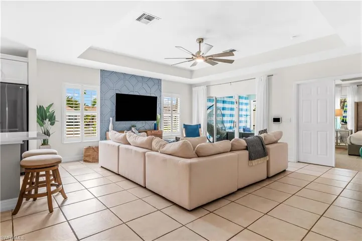 Spacious open-concept living area featuring light-toned tile flooring, a tray ceiling with a ceiling fan, and sliding glass doors to the exterior