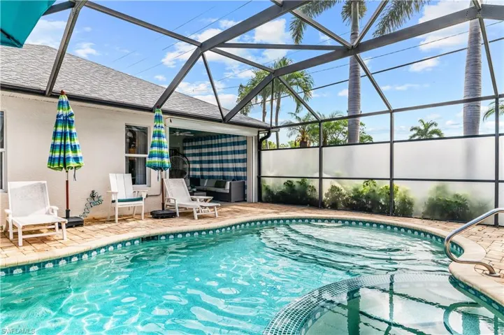 Screened pool enclosure featuring a curved pool with an integrated spa, brick paver decking, and a covered lanai