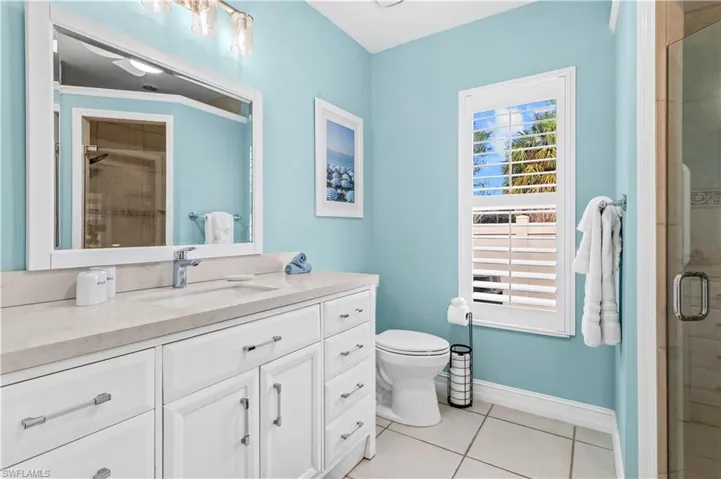 Bathroom featuring a long single vanity with an integrated sink, a large framed mirror, and a window with plantation shutters