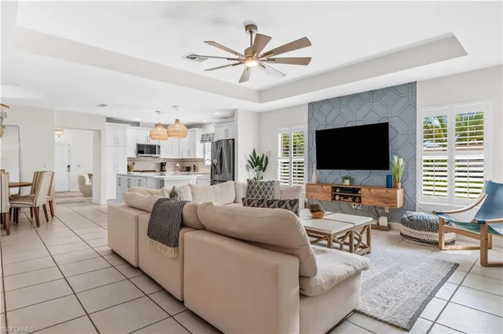 Living area featuring a detailed accent wall with geometric patterning, a tray ceiling, and a ceiling fan