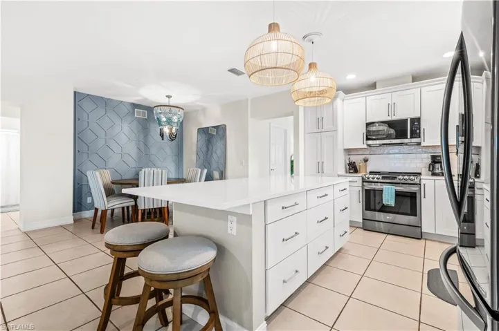 Open-concept kitchen featuring a large central island with seating, white shaker cabinetry, stainless steel appliances, and a subway tile backsplash