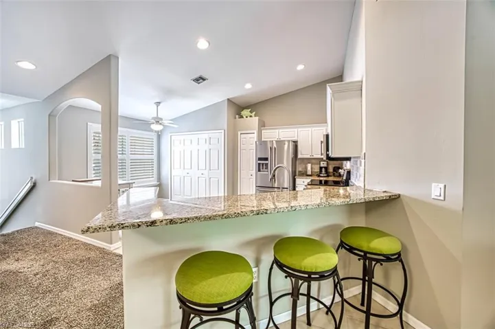 Kitchen with vaulted ceiling, stainless steel fridge with ice dispenser, kitchen peninsula, a kitchen breakfast bar, and white cabinets