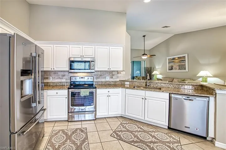 Kitchen with appliances with stainless steel finishes, white cabinets, dark stone counters, sink, and ceiling fan