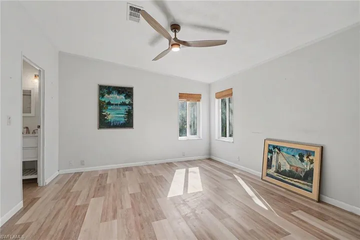 Master bedroom with en-suite bath and light wood-type flooring, ceiling fan, vaulted ceiling, and crown molding.
