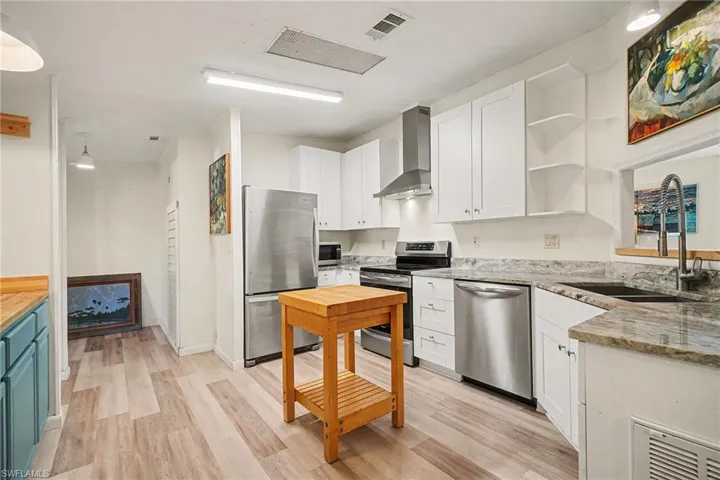 Kitchen featuring open shelves, stainless steel appliances, wall chimney range hood, light wood finished floors, and white cabinets
