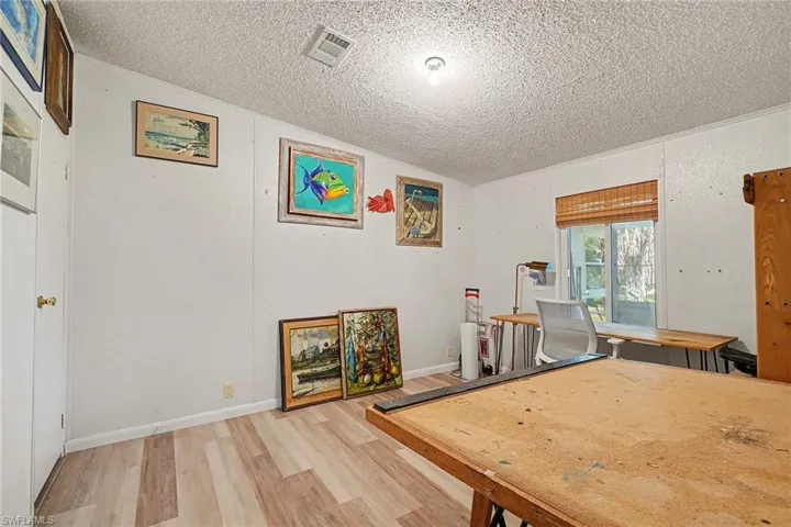 Third bedroom with light wood-type flooring and a textured ceiling.  Used as a studio/office overlooking the expansive property.