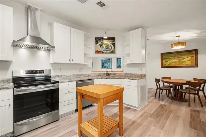 Kitchen featuring appliances with stainless steel finishes, wall chimney exhaust hood, white cabinets, and open shelves