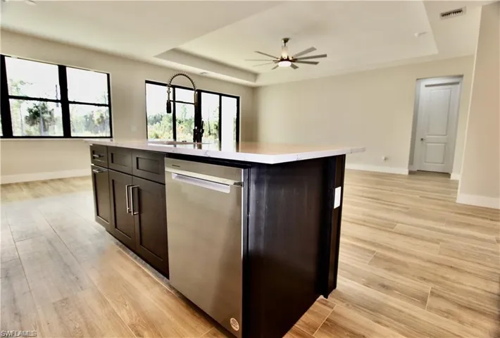 Kitchen with ceiling fan, dishwasher, a raised ceiling, and an island with sink