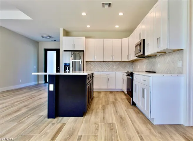 Kitchen with range with electric cooktop, a kitchen island with sink, light wood-type flooring, white cabinets, and sink