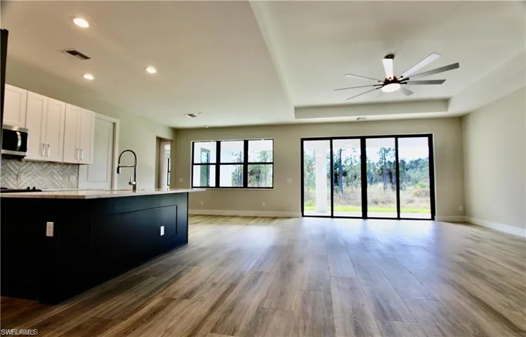 Kitchen with ceiling fan, tasteful backsplash, light wood-type flooring, white cabinets, and sink