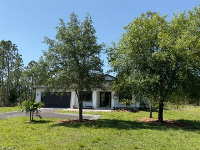 View of property hidden behind natural elements featuring a front lawn and a garage