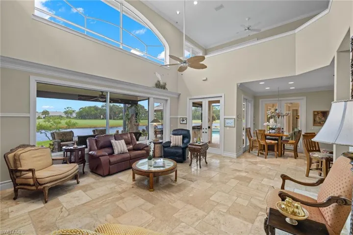 Living room featuring a water view, crown molding, ceiling fan, a towering ceiling, and french doors
