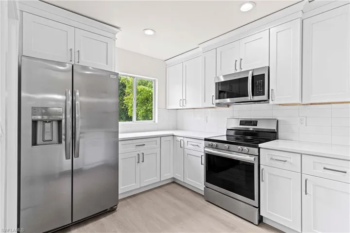 Kitchen with light hardwood / wood-style floors, tasteful backsplash, white cabinetry, and appliances with stainless steel finishes