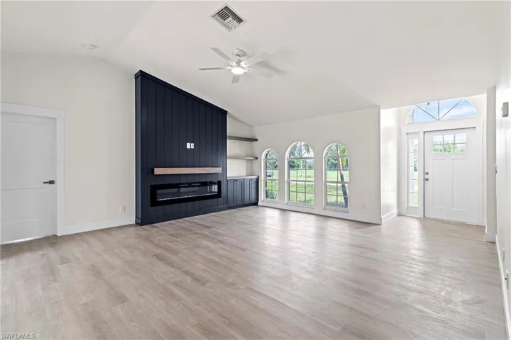 Unfurnished living room with vaulted ceiling, ceiling fan, light wood-type flooring, and a fireplace