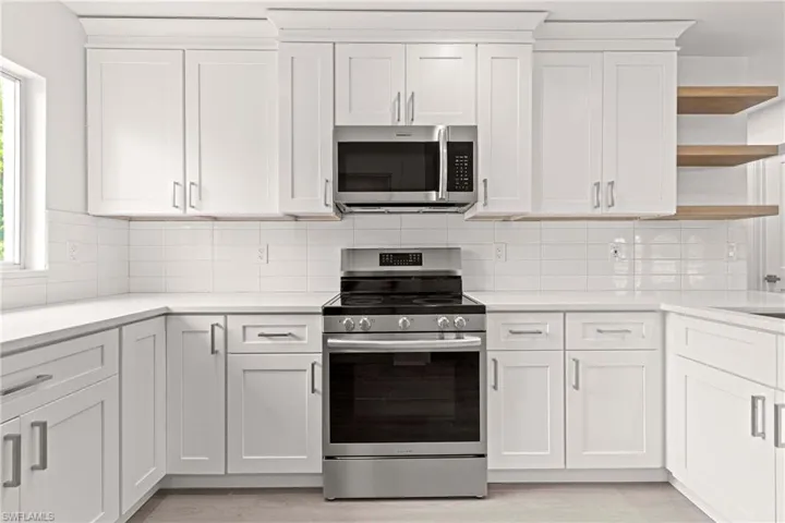 Kitchen with a wealth of natural light, tasteful backsplash, white cabinetry, light wood-type flooring, and appliances with stainless steel finishes