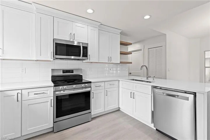 Kitchen featuring tasteful backsplash, light wood-type flooring, sink, white cabinetry, and appliances with stainless steel finishes