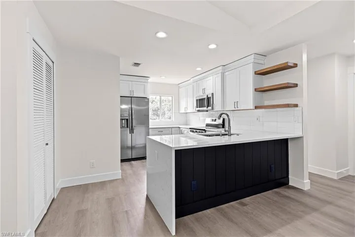 Kitchen with light hardwood / wood-style floors, white cabinetry, stainless steel appliances, kitchen peninsula, and sink